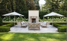 an outdoor fireplace surrounded by lawn chairs and tables with umbrellas on top of it