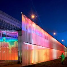 a person standing in front of a building with rainbow lights on it's side