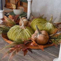 green velvet pumpkins and greenery in a bowl on a dining room table with fall leaves