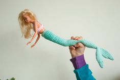 a hand holding a doll in the shape of a mermaid tail