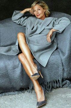 a woman sitting on top of a couch covered in a gray blanket and wearing high heels