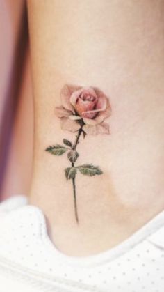 a small rose tattoo on the side of a woman's rib - up stomach