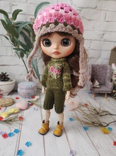 a doll is wearing a knitted hat and green pants with pink flowers on it