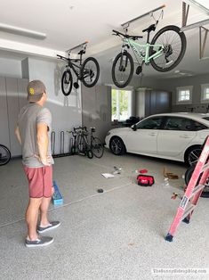 a man standing next to a car in a garage with two bikes hanging from the ceiling