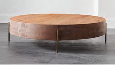 a round wooden table with metal legs on concrete flooring and white walls in the background