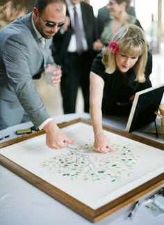 a man and woman are looking at something on a table with other people in the background