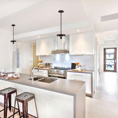 a large kitchen with white cabinets and stainless steel counter tops, along with bar stools