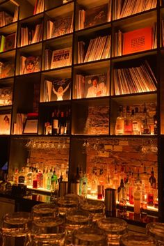 shelves filled with liquor bottles and glasses in front of an assortment of books on the wall