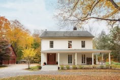 a white two story house surrounded by trees and leaves in the fall with autumn foliage on the ground