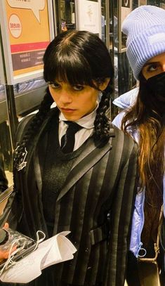 two women in black and white outfits standing next to each other on a subway platform