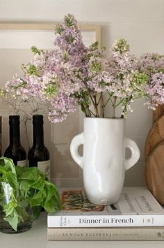 a white vase filled with flowers on top of a table next to books and bottles