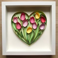 a paper heart with flowers cut out of it in a white frame on a wooden table