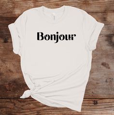 "**Order by December 11 to receive in time for Christmas Elevate your fashion game with our trendy \"Bonjour\" T-shirt - a stylish fusion of French charm and modern elegance. This iconic tee showcases the word \"Bonjour\" in a beautifully designed serif font, adding a touch of Parisian flair to your wardrobe. Crafted from premium, comfortable cotton fabric, it's the ideal choice for those who appreciate both style and comfort. Say \"hello\" to a new level of fashion with this chic and fashionable tee. Embrace the elegance of \"Bonjour\" and make a statement wherever you go! 🛒 HOW TO ORDER SHIRT 1) Please, Check and Review all Photos. 2) Select Your T-Shirt Size and T-Shirt Color from drop-down menus. 3) Choose Your Quantity as much as you want. 4) Click ADD TO CART. And, you can go back t Trendy Slogan T-shirt As Gift, Trendy Graphic Print Shirt As Gift, Trendy Slogan Tops For Gifts, Trendy Crew Neck Shirt As A Gift, Trendy Crew Neck Shirt As Gift, Trendy Text Print Top As Gift, Trendy Screen Print T-shirt For Gifts, Trendy White Shirt As A Gift, Paris Shirt