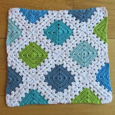 a crocheted square on a wooden floor with a blue and green design in the middle