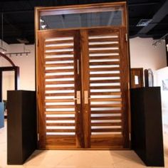 an open wooden door in the middle of a room with black pedestals and white walls