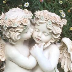 two white cherubs with their heads touching each other in front of some daisies