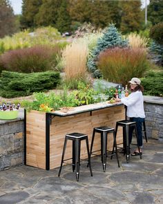 a woman standing at a bar made out of wood and metal with plants growing in it