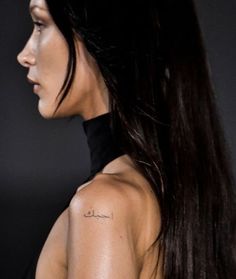 the back of a woman's shoulder with arabic writing on her left upper arm