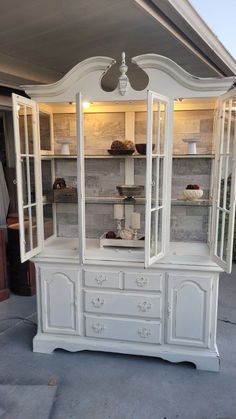 a white china cabinet with glass doors and drawers on the top, in front of a house