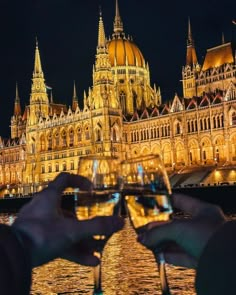 two people toasting with glasses in front of a large building at night, while the lights shine brightly on them