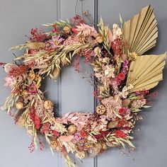 a wreath is hanging on the door with dried flowers and fan shaped leaves around it