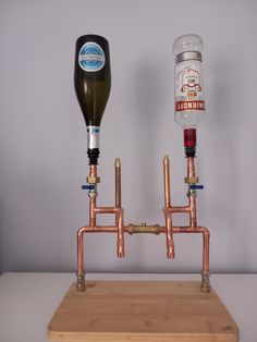 two copper pipes connected to each other on top of a wooden block with a bottle in the middle