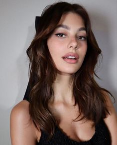 a woman with long brown hair wearing a black dress and posing for the camera in front of a white wall