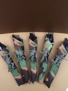 five forks and four knives are wrapped in camouflage fabric with soldiers on them, sitting next to each other