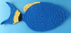 a crocheted blue and yellow fish decoration on a blue tablecloth with the shape of a fish