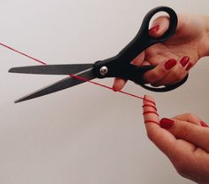 a pair of hands holding scissors with red string attached to the handle and two fingers