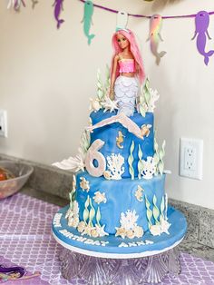 there is a cake with a barbie doll on it and decorations around the top tier