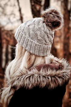 a woman with long blonde hair wearing a knitted hat and fur coat in the woods