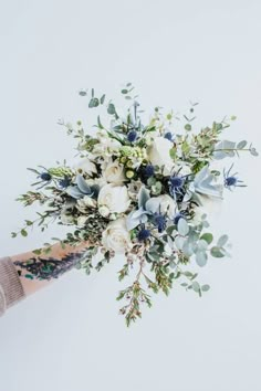 a bridal bouquet with white flowers and greenery on the stems is being held by someone's hand