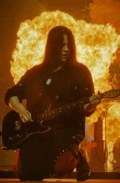 a man sitting on the ground playing a guitar in front of a large fireball