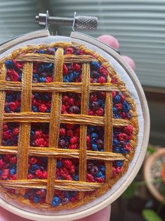 a hand holding a small piece of art made out of yarn and wood with red, white and blue squares on it