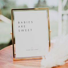 a sign that says babies are sweet on top of a wooden table next to feathers