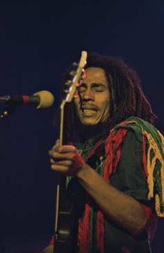 a man with dreadlocks holding a guitar in front of a microphone on stage