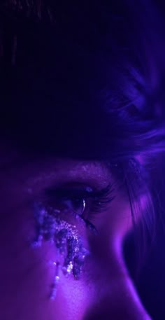 a woman's eye with purple light shining on her face and the bottom part of her eyelashes