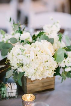 white flowers and greenery sit in a wooden vase on a table with silverware