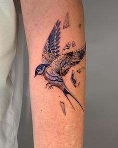 a blue bird flying through the air with an arrow in its beak tattoo on someone's leg