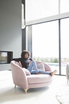 a woman sitting on a pink chair in front of a window