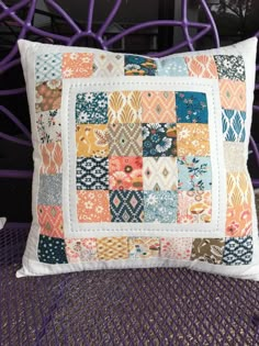 a pillow made out of colorful patchwork on top of a purple chair with white piping