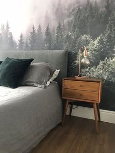 a bedroom with a bed, night stand and wallpaper that has trees on it