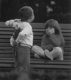 two young children sitting on a bench with flowers in their hands and one holding a flower