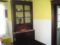 an empty room with yellow walls and wooden furniture in it, including a china cabinet