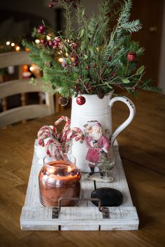 a white pitcher filled with greenery sitting on top of a table next to a candle