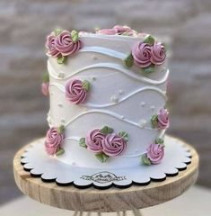 a white cake with pink roses on it sitting on top of a wooden stand next to a brick wall