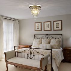 a bed sitting next to a window in a bedroom under a chandelier with pictures on the wall