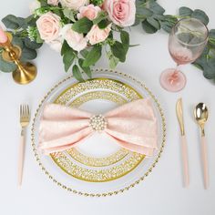 the table is set with pink flowers and gold place settings, such as silverware