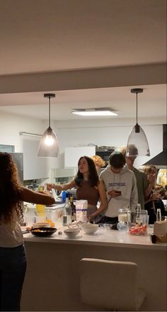 a group of people standing around a kitchen counter with food on top of it and drinks in front of them